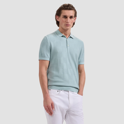 Man wearing a light blue polo shirt and white pants on a plain background