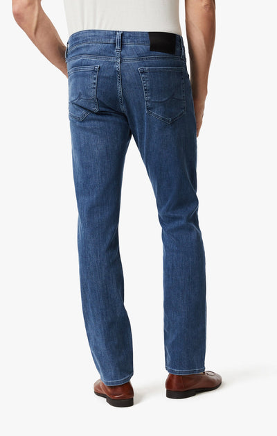 A man is shown from the back against a white background wearing 34 Heritage Mid Urban straight-leg, dark-wash jeans by 34 Heritage, paired with brown shoes and a white shirt.
