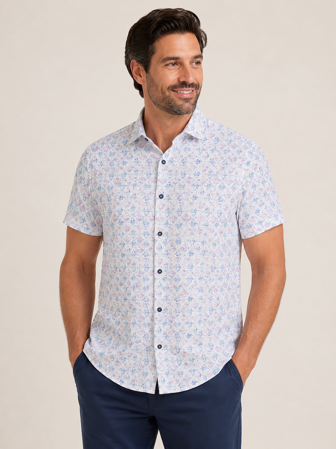 A man stands with his hands in his pockets against a plain background, wearing the Robert Graham Greatorex Woven Shirt Big & Tall—a short-sleeve, light-colored stretch cotton button-up with an allover print—paired with dark pants.