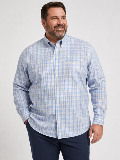 A man is wearing the Tailor & Mason T55-126T Long Sleeve Check Shirt, featuring a blue and grey plaid design in non-iron cotton, paired with dark blue pants. He stands smiling against a plain light background.