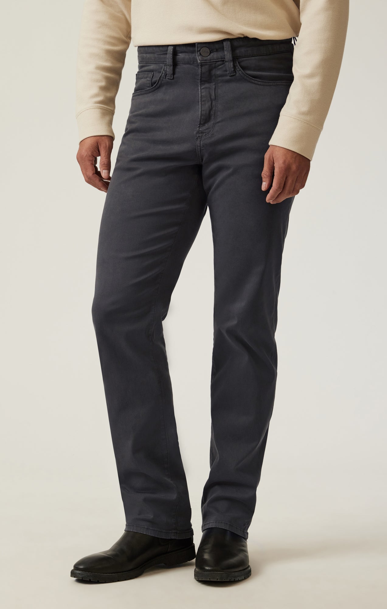 A person wearing a cream long-sleeve shirt, black boots, and 34 Heritage Ash Twill dark gray straight-leg trousers stands against a plain light background.