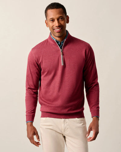 A man models the Johnnie-O Sweater SULLY 1/4 Zip over a blue button-down shirt and light-colored pants, standing against a plain background.