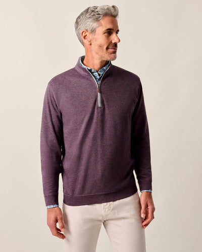Man with short gray hair wears the Johnnie-O Sweater SULLY 1/4 Zip in purple over a patterned shirt and light-colored pants, standing against a plain background.