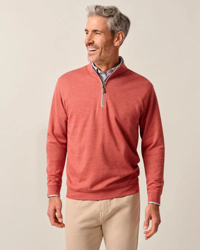 A man wearing the Johnnie-O Sweater SULLY 1/4 Zip stands against a plain background, smiling and looking to his left. He pairs the red quarter-zip pullover with a light blue collared shirt and beige pants.