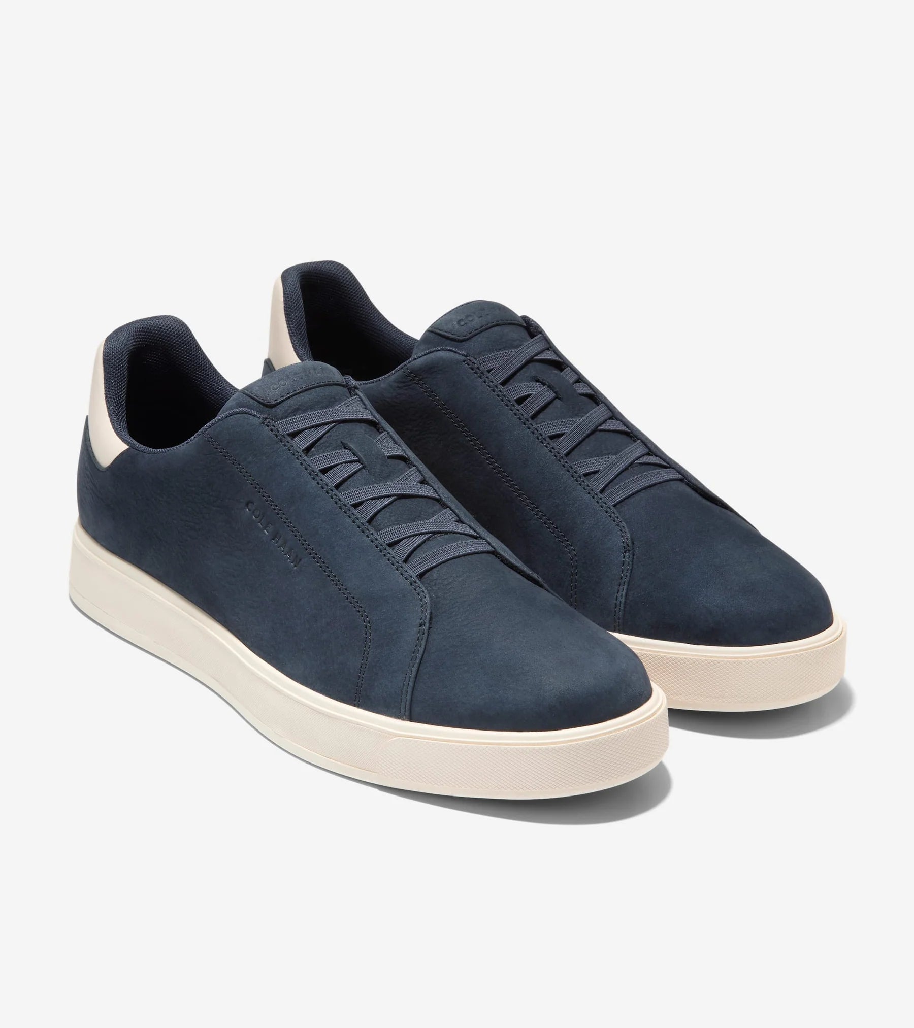 The Cole Haan GrandPro Luxe Slip On Sneaker is a navy blue low-top with white soles, minimal branding, and FlowerFoam™ cushioning for comfort, shown on a plain white background.