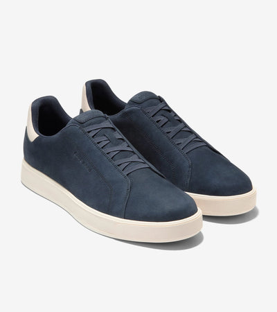 The Cole Haan GrandPro Luxe Slip On Sneaker is a navy blue low-top with white soles, minimal branding, and FlowerFoam™ cushioning for comfort, shown on a plain white background.