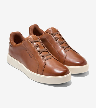 The Cole Haan GrandPro Luxe Slip On Sneaker by Cole Haan features brown leather, white rubber soles, and FlowerFoam cushioning, shown against a light background.