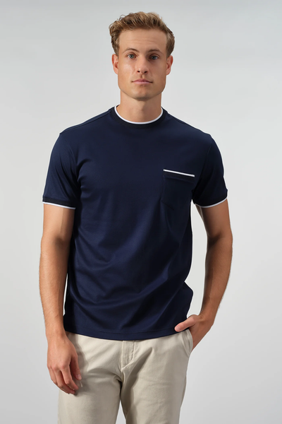 A man stands against a plain background wearing the Garnet Setatouch Pocket Tee 2617011CC by Garnet, a navy blue short-sleeve t-shirt with white trim and chest pocket, paired with light beige pants.