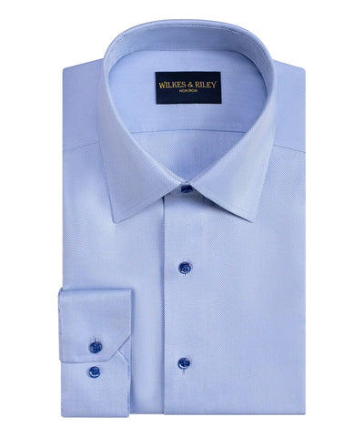 The Wilkes & Riley Herringbone Dress Shirt in light blue is made of Supima cotton, features a pointed collar, blue buttons, and a wrinkle-free, non-iron finish for easy care.