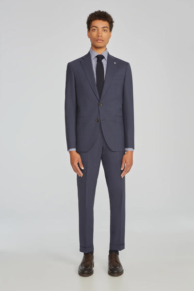 A person stands facing forward against a plain light background, wearing the Jack Victor Wool Stretch Suit by Jack Victor, paired with a light blue dress shirt, dark tie, and dark dress shoes.