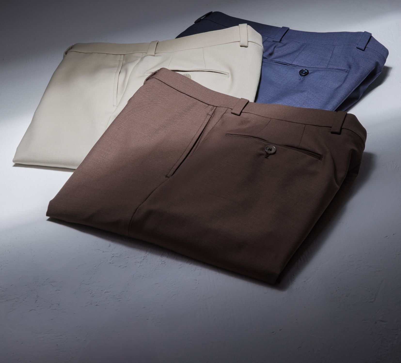 A selection of Jack Victor Riviera Traveler Pants in various solid colors, including blue, tan, and brown, displayed in an arranged pile with the focus on the design and color variety.