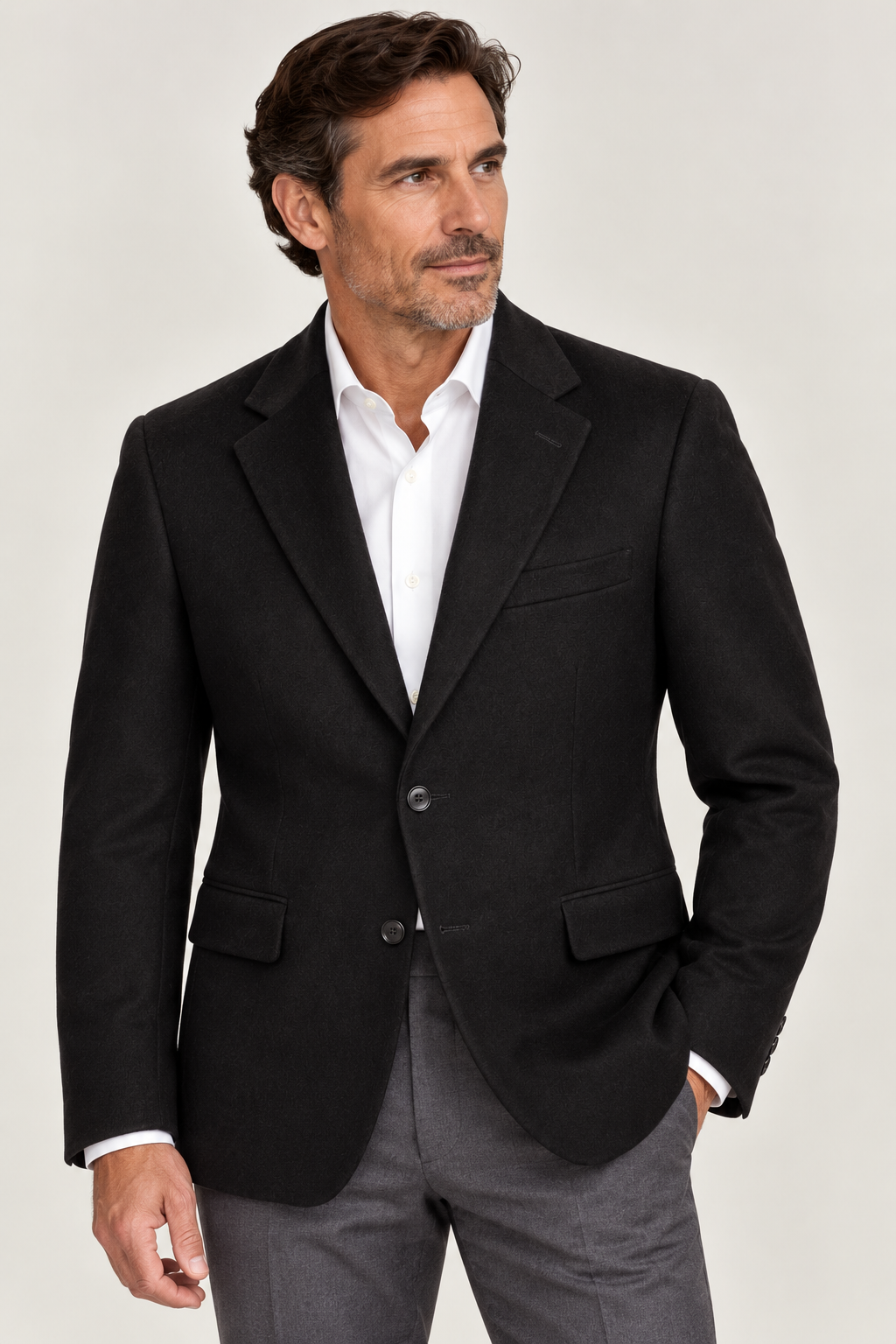 A man wearing the Giles & Jasper Cashmere Sport Coat by Giles & Jasper, paired with a white dress shirt and gray pants, stands with one hand in his pocket, looking to the side against a plain background.