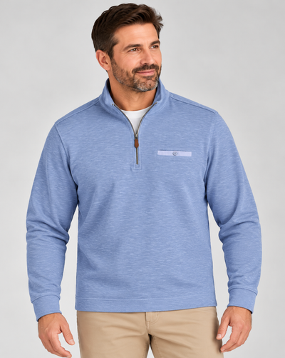 A man wearing a light blue Johnnie-O Flame Stitch 1/4 Zip Sweater Big & Tall with a small chest pocket and khaki pants.