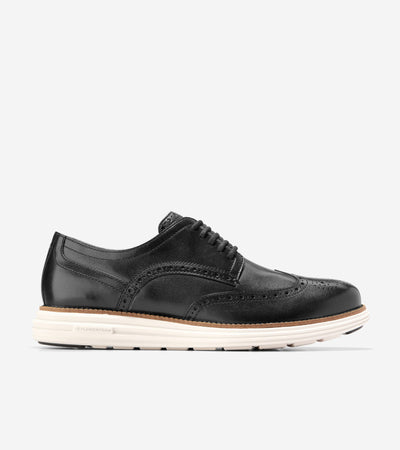 The Cole Haan Grand Remastered Wingtip Oxford from Ted's Clothiers features a black brogued leather upper, FlowerFoam midsole, and white rubber sole, displayed in profile against a plain background.