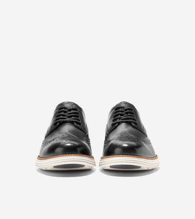 A pair of black Cole Haan Grand Remastered Wingtip Oxford shoes from Ted's Clothiers, featuring a brogued leather upper and a white FlowerFoam midsole, shown from the front on a plain white background.