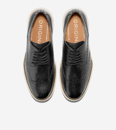 A pair of black leather Cole Haan Grand Remastered Wingtip Oxford shoes from Ted's Clothiers, featuring tan ORIGIN-labeled insoles and white FlowerFoam midsoles, viewed from above on a white background.