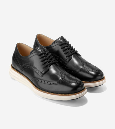 The Cole Haan Grand Remastered Wingtip Oxford by Ted's Clothiers features a black brogued leather upper, white rubber soles, black laces, and refined detailing. Displayed on a plain light background, it’s inspired by the ØriginalGrand Remastered Shortwing style.