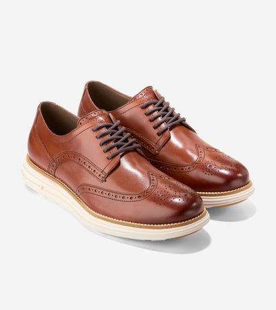 A pair of brown Cole Haan Grand Remastered Wingtip Oxfords from Ted's Clothiers, featuring a brogued leather upper, dark laces, and white midsoles, is displayed on a plain background.