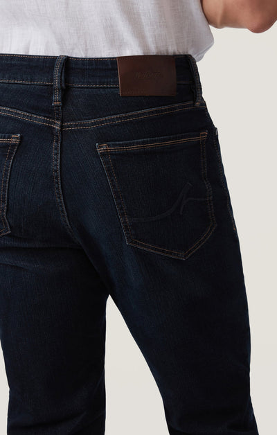 Model wears the 34 Heritage Dark Comfort jeans by 34 Heritage—a higher-rise, five-pocket dark blue style—paired with a white shirt, shown from the back to highlight the rear pockets and waistband.