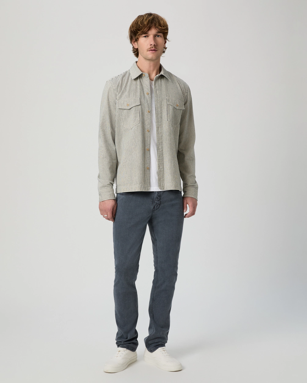 Man wearing a light gray shirt and dark blue jeans on a white background