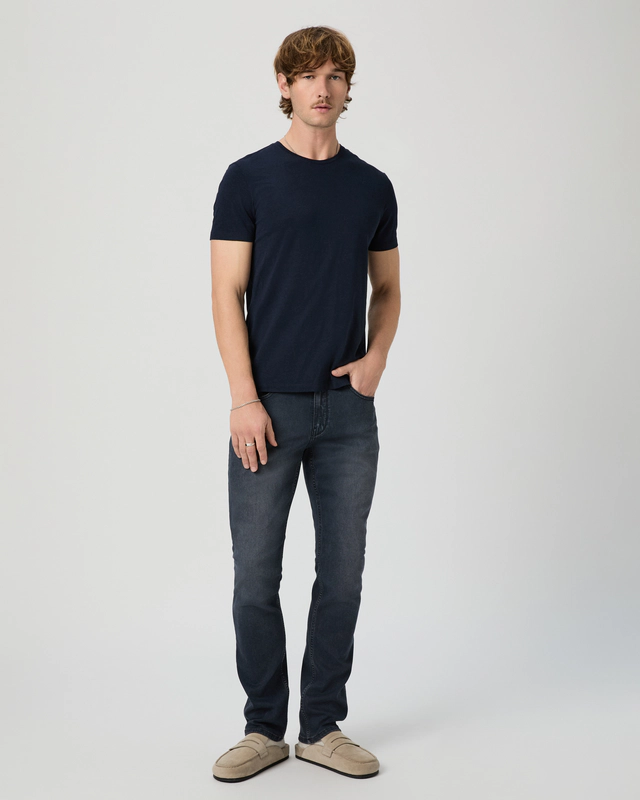 Man wearing a navy t-shirt and dark jeans on a white background