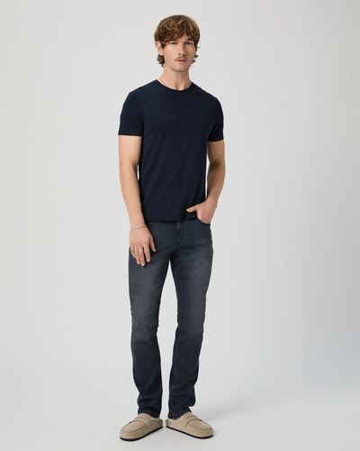 Man wearing a navy t-shirt and dark jeans on a white background