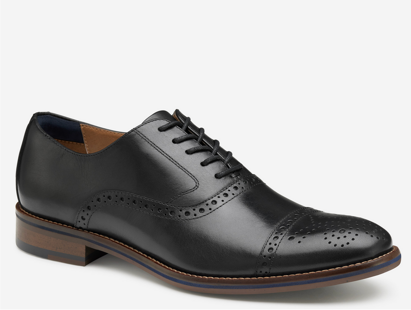 The Johnston & Murphy Conard 2.0 Cap Toe is a black leather men’s Oxford dress shoe with brogue detailing, cushioned comfort, and a brown sole, pictured on a white background.