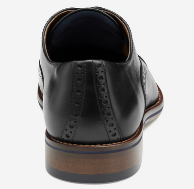 Rear view of the Johnston & Murphy Conard 2.0 Cap Toe in black leather, featuring decorative perforations, a stacked heel with wood and blue accents, and designed for cushioned comfort by Johnston Murphy.