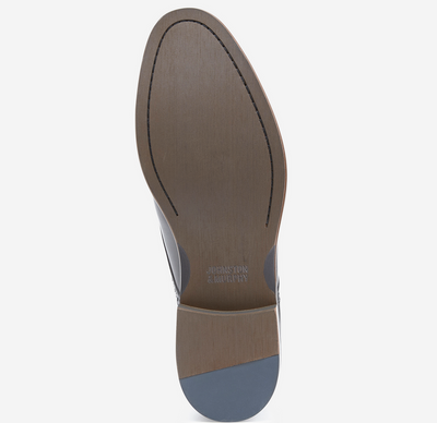 The image shows the bottom view of the Johnston & Murphy Conard 2.0 Cap Toe, featuring a leather sole with visible stitching and Johnston Murphy branding near the arch, combining classic style with cushioned comfort.
