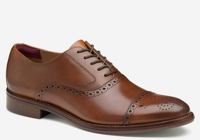 The Johnston & Murphy Conard 2.0 Cap Toe is a brown leather dress shoe featuring brogue details, cushioned comfort, closed lacing, and a low wooden heel, shown on a plain white background.