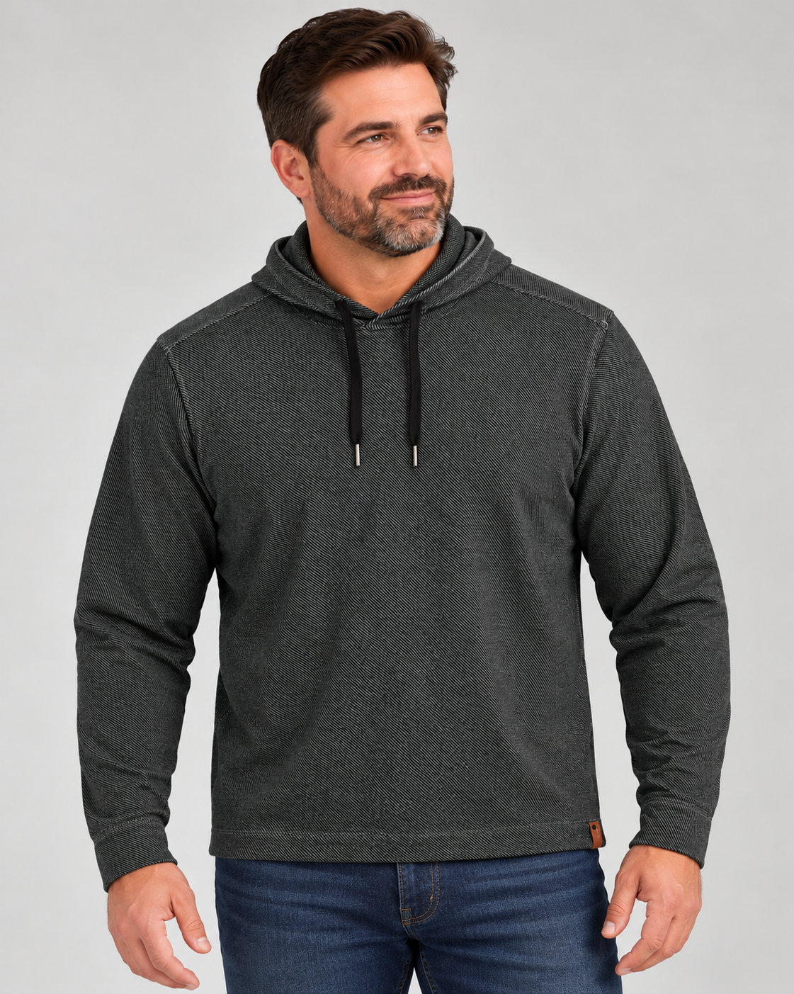 A man wearing a black long-sleeve Tommy Bahama Fireside Coast Hoodie with black drawstrings and blue jeans.