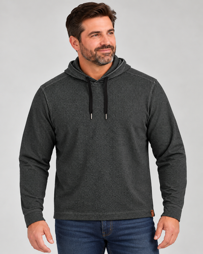 A man wearing a black long-sleeve Tommy Bahama Fireside Coast Hoodie with black drawstrings and blue jeans.