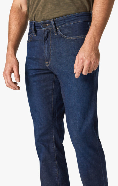 A person wearing a green shirt and 34 Heritage Dark Cashmere high rise jeans by 34 Heritage, shown from waist to mid-thigh, standing against a plain background.