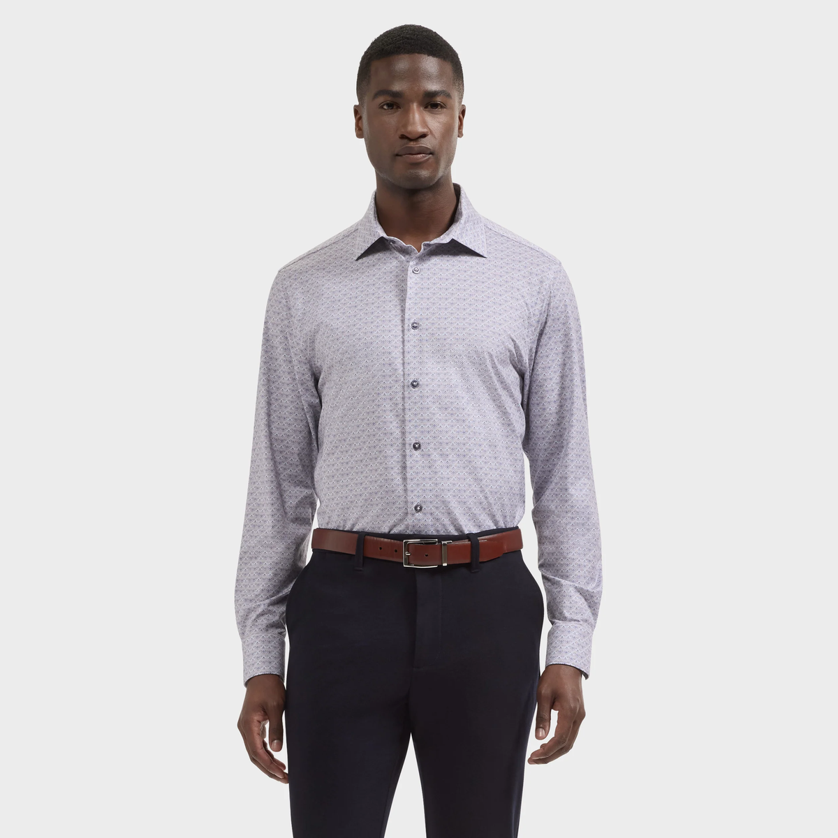 A man wearing the Bugatchi James Medallion Sport Shirt KF9062K60, renowned for its breathable and wrinkle-resistant OoohCotton fabric, paired with dark trousers and a brown belt, stands against a plain white background.
