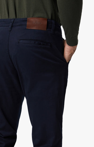 A person wearing 34 Heritage Charisma Navy Twill Jeans with a brown leather patch on the waistband and an olive green long-sleeve shirt, one hand in their pocket.