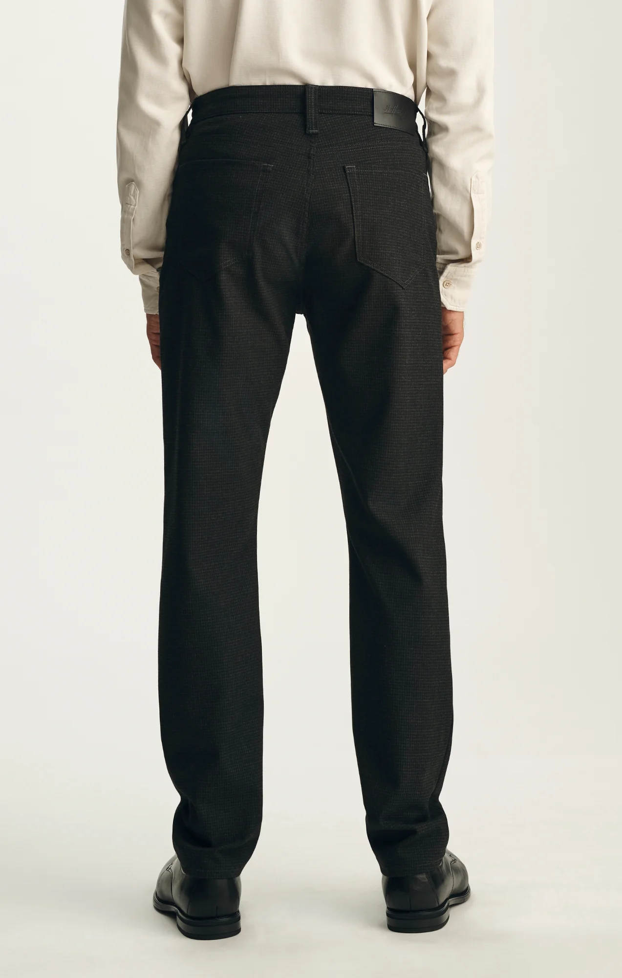 A man stands with his back to the camera against a plain background, wearing the 34 Heritage Courage Supreme Plaid trousers by 34 Heritage paired with a white shirt and black shoes.
