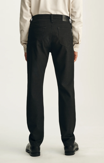 A man stands with his back to the camera against a plain background, wearing the 34 Heritage Courage Supreme Plaid trousers by 34 Heritage paired with a white shirt and black shoes.