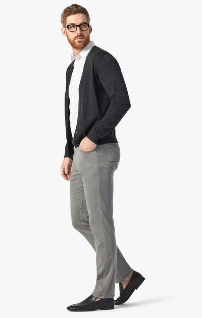 A man in a black cardigan, white shirt, 34 Heritage Pewter Twill relaxed straight-leg gray pants, and black loafers stands against a plain white background.