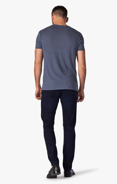 A man faces away, wearing the 34 Heritage Ink Urban straight leg dark-wash jeans, a short-sleeve blue t-shirt, and black shoes against a plain white background.