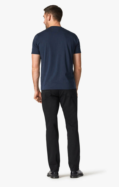 Man with his back to the camera, wearing a navy short-sleeve t-shirt, 34 Heritage Double Black pants by 34 Heritage with a relaxed thigh, and black shoes against a plain white background.