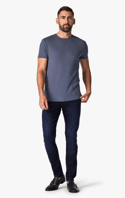 A man stands facing forward wearing 34 Heritage Ink Urban dark-wash modern straight leg jeans, a short-sleeve blue t-shirt, and black loafers against a plain white background.