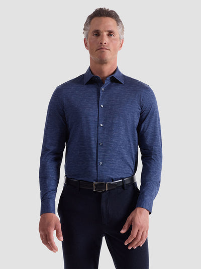 A man faces forward in a Bugatchi James Long Sleeve Shirt HF9505K60 by Bugatchi, paired with black pants and a black belt, showcasing refined menswear style against a plain light background.
