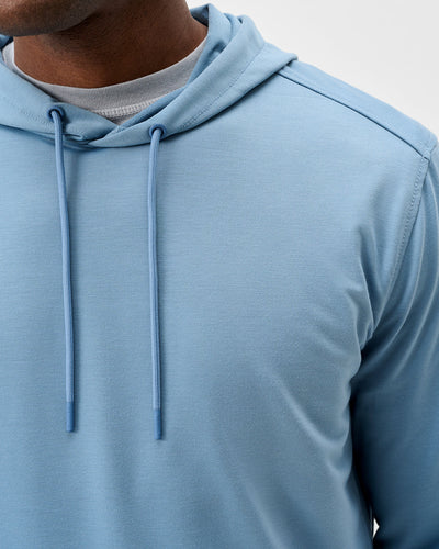 A person wearing the Johnnie-O Willard Performance Hoodie Big & Tall in light blue, featuring drawstrings and layered over a gray shirt, is shown from the chest up. This athletic fit hoodie by Johnnie-O offers moisture-wicking fabric for all-day comfort.