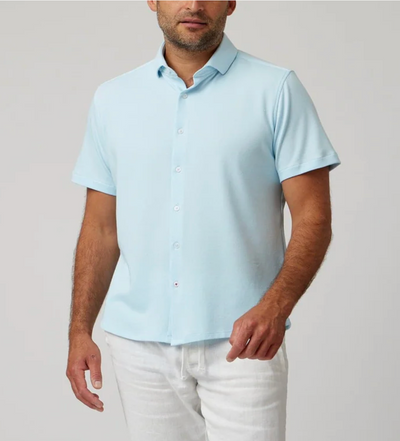 A man wears the Stone Rose SS Pique Shirt 2K7T241 in light blue with white pants, standing against a plain light background.