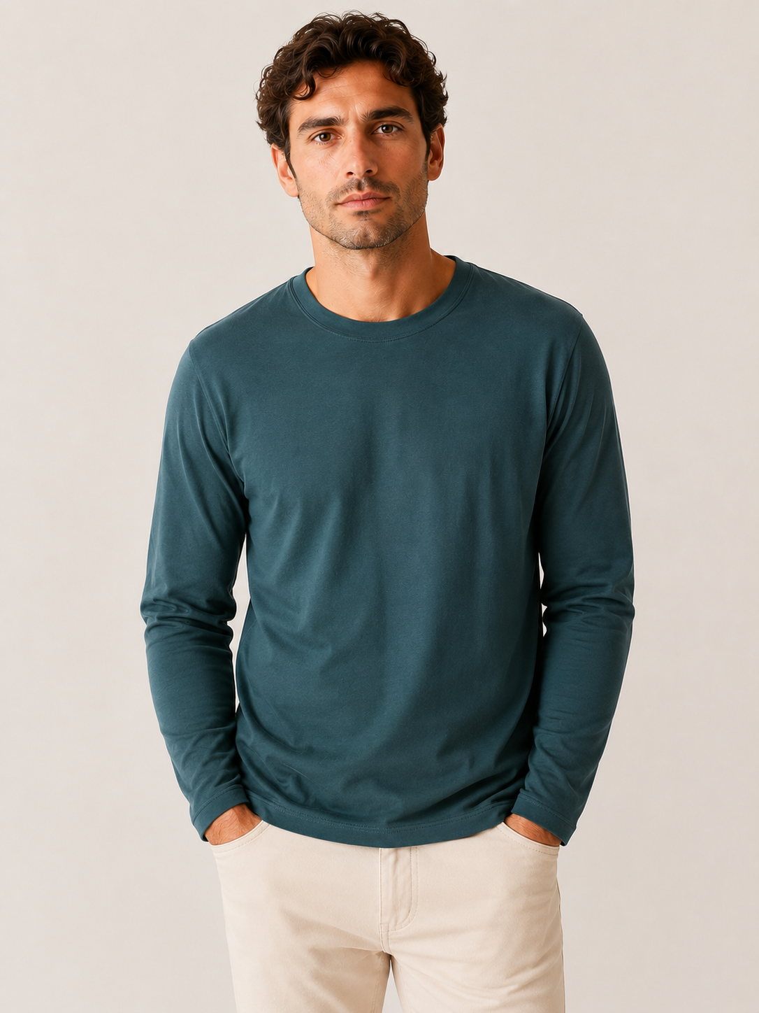 A man wearing a teal Robert Barakett High Crew Long Sleeve RB82247 and light beige pants stands with his hands in his pockets against a plain background.