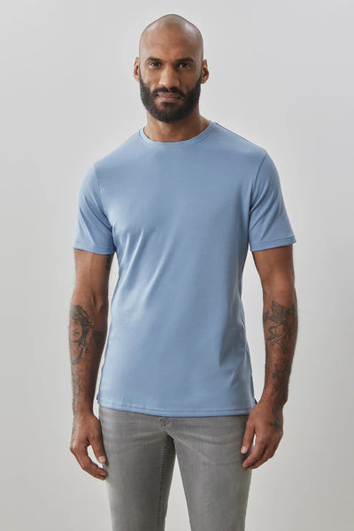 A bearded, tattooed man stands against a plain light background wearing the Robert Barakett Georgia Crew 23336 Tee Shirt in light blue and light gray jeans.