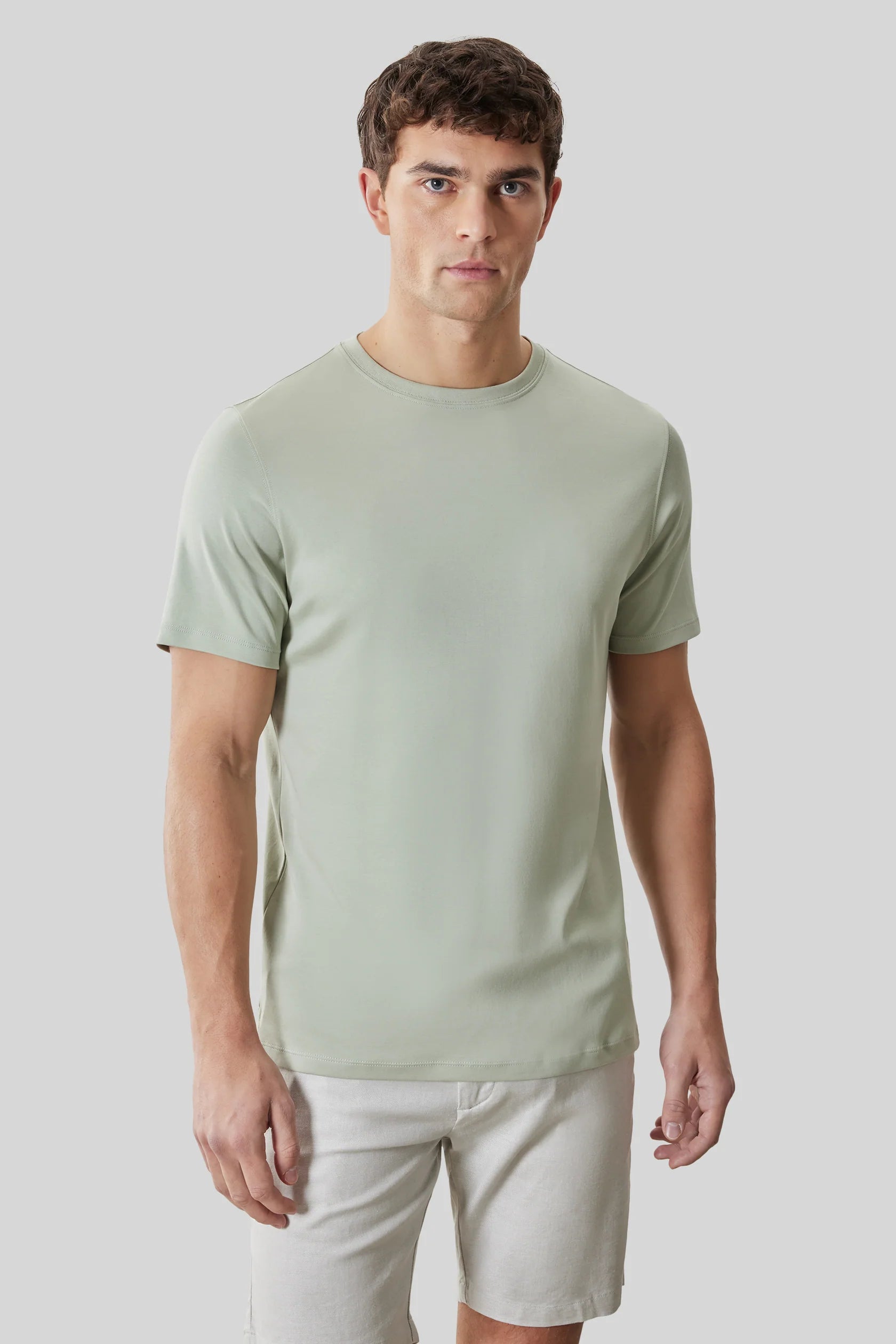 A man stands against a gray background wearing the Robert Barakett Tee Shirt Georgia Crew 23336 by Robert Barakett in light green and light-colored shorts.
