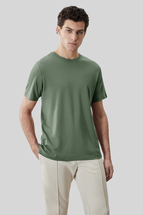 A man stands against a plain grey background wearing a sage green Robert Barakett Tee Shirt Georgia Crew 23336 and light beige pants, with one hand in his pocket.