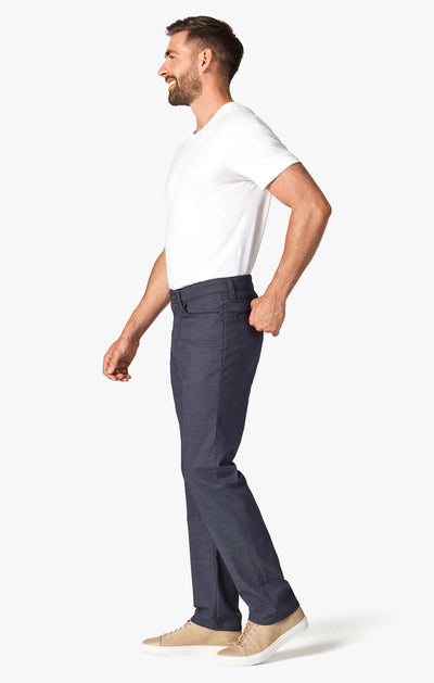 A man stands in profile wearing a white t-shirt, 34 Heritage Navy Coolmax temperature-regulating pants by 34 Heritage, and beige sneakers against a plain white background.