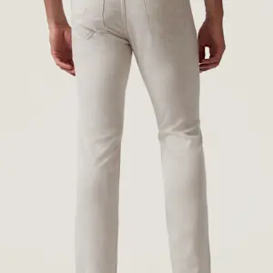 A person is shown from the waist down, standing with their back to the camera against a neutral background, wearing light-colored 34 Heritage Courage Cross Twill pants by 34 Heritage.